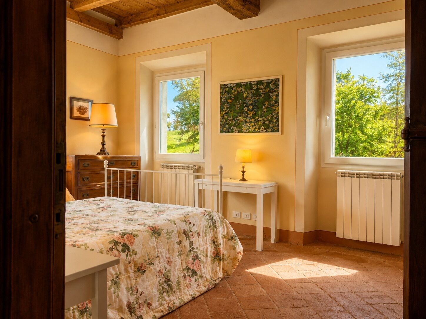 A bedroom with a bed, a nightstand, a dresser, a window with a view of greenery, and a painting on the wall.