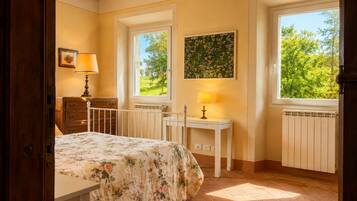 A bedroom with a bed, a nightstand, a dresser, a window with a view of greenery, and a painting on the wall.