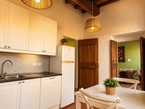 A kitchen with white cabinets, a black countertop, and a white refrigerator. There is a wooden door and a table with a plant.