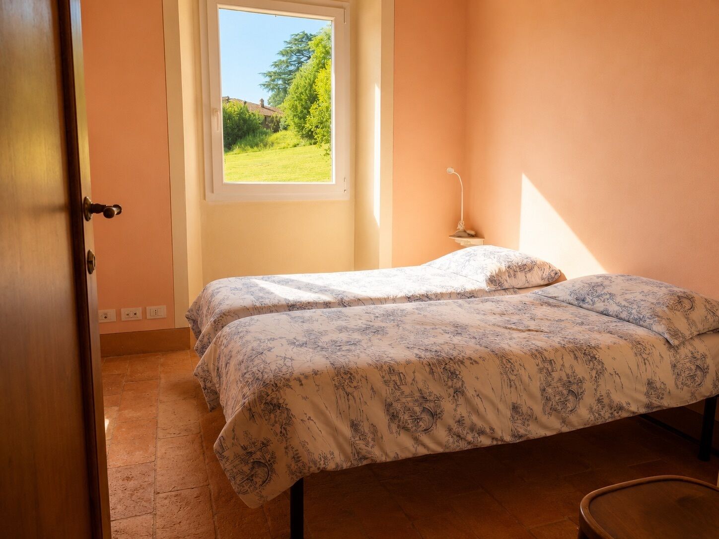 Ein Schlafzimmer mit zwei Betten, einem Fenster mit Blick auf Grünflächen und einer Tür.