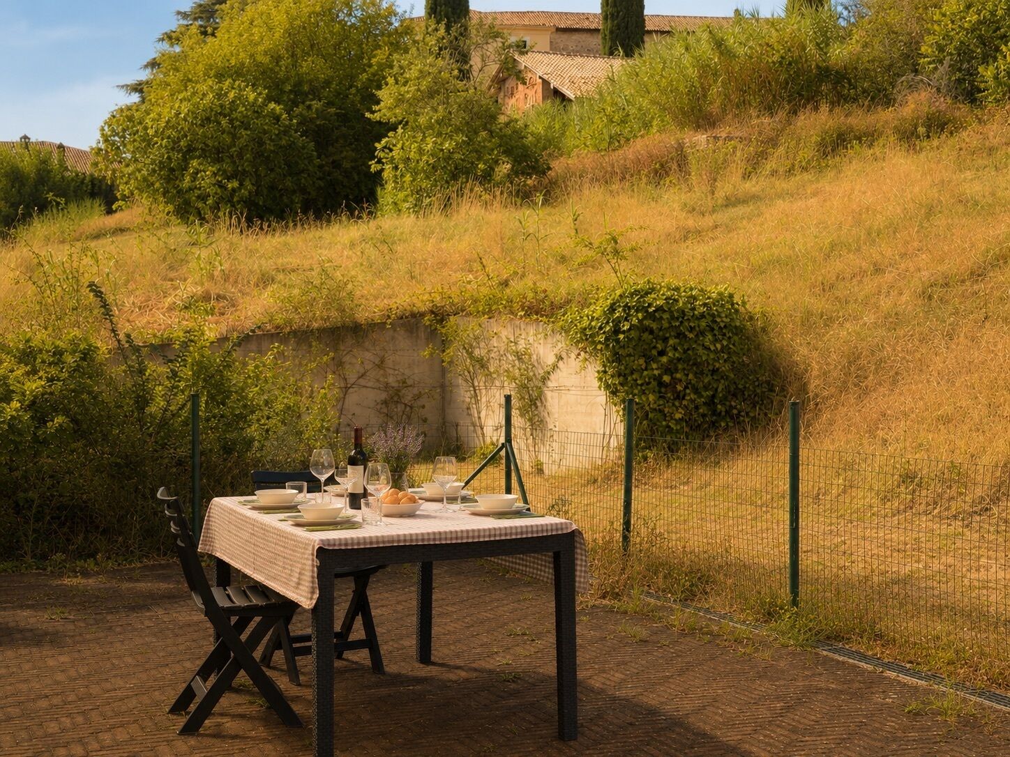 An outdoor dining area with a table set for two, surrounded by a natural landscape and a fence.