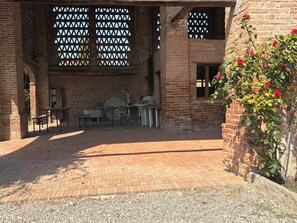 An outdoor patio area with brick flooring, a table with chairs, and a rose bush.