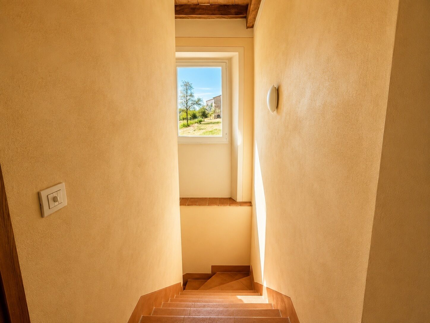 A narrow stairway leading to a landing with a window overlooking a landscape.