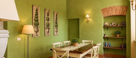 A dining area with a green wall, wooden ceiling beams, a table with chairs, and a lamp.