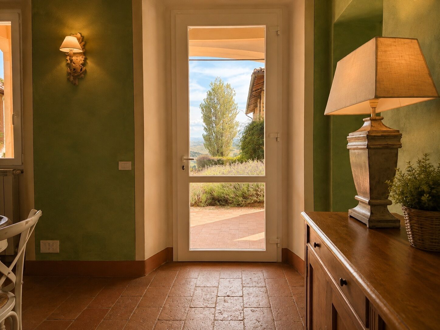Una habitación con una puerta que da a un espacio exterior, una lámpara en la pared y una mesa de madera.