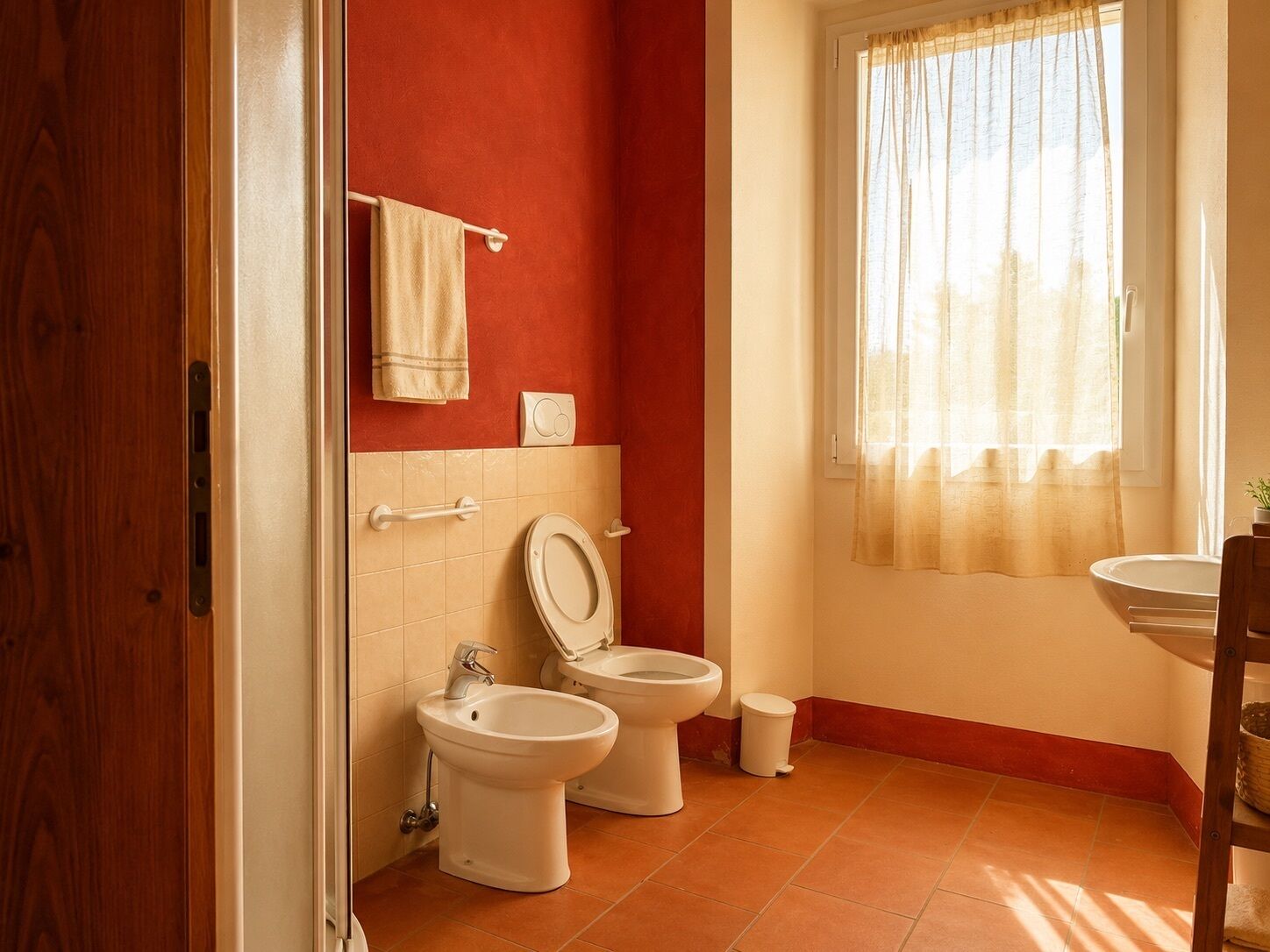 Un bany amb dues vàteres, un bidet, un lavabo i una finestra amb cortines.