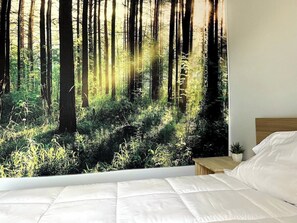 Um quarto com um grande mural temático de floresta, uma cabeceira de madeira e uma cama bem arrumada.