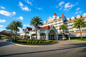 Un grande hotel con diversi piani, un ingresso ben visibile, palme e un cielo azzurro.