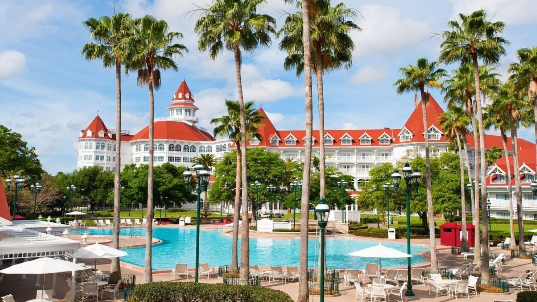 A resort with a large pool, palm trees, and a building with red roofs.
