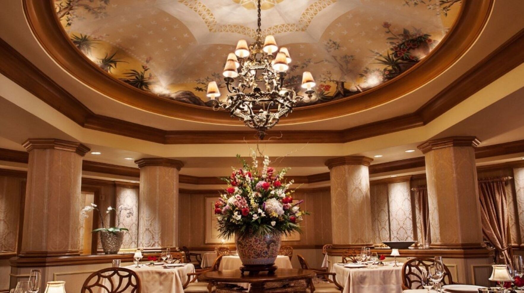 A formal dining room with a chandelier, floral centerpiece, and classic decor.
