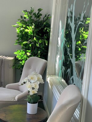 A room with a beige armchair, a small round table with a potted plant, and a large mirror reflecting greenery. - Eagle - Private Bedroom near Downtown and 17th Av (Calgary)