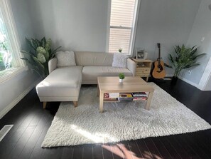 Ein Wohnzimmer mit Ecksofa, Couchtisch, Gitarre und einem weißen Shaggy-Teppich.