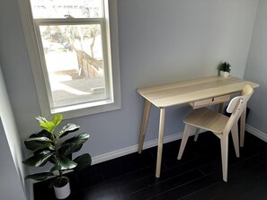 Ein Zimmer mit Schreibtisch, Stuhl, Blumentopf und Fenster.