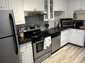 Cocina moderna con armarios blancos, un refrigerador de acero inoxidable, una encimera negra y un microondas.