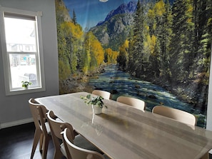 A dining area with a table and chairs, a window with a view of a building, and a mural of a river and forest. - Bear - Private Master Bedroom near DT and 17th Av (Calgary)