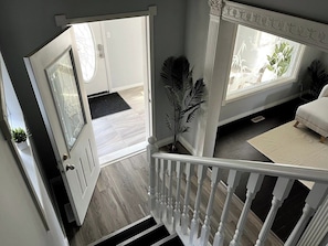 A staircase leading to a room with a white railing, a door with glass panels, and a window with a view of greenery. - Bear - Private Master Bedroom near DT and 17th Av (Calgary)