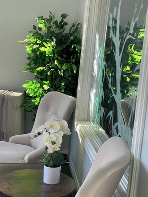 A room with a white armchair, a small round table with a potted plant, and a large mirror reflecting greenery. - Wolf - Private Bedroom near Downtown and 17th Av (Calgary)