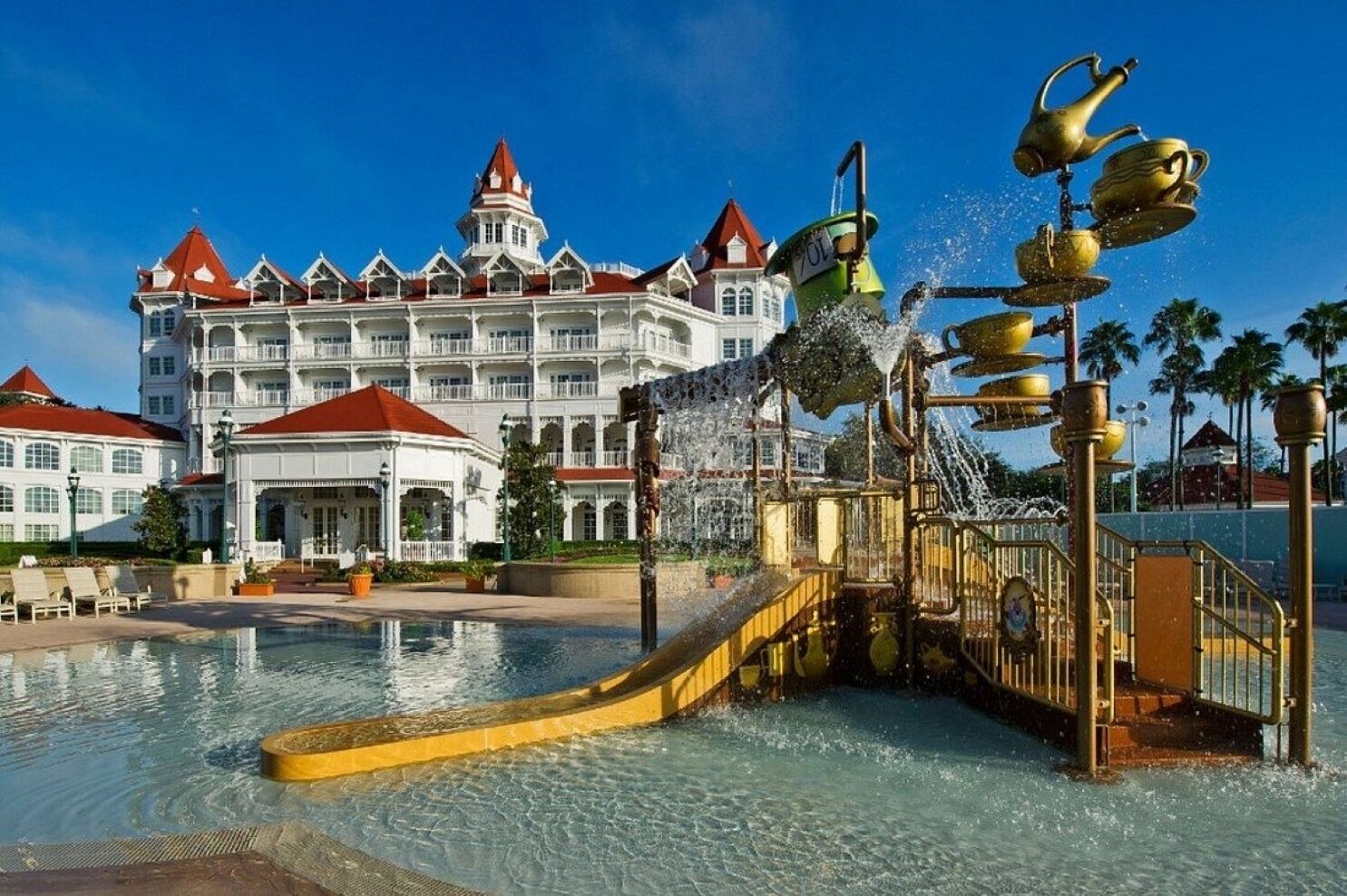 A hotel with a large pool, a water fountain with golden cups, and a grand building with multiple balconies and a red roof.