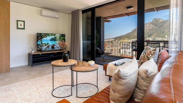 A modern living room with a flat-screen TV, a sofa, a coffee table, and a balcony with a view of a mountain. - Breathtaking Apt, Mountain Views - Bo-Kaap Retreat (Cape Town)