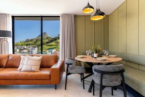 Ein modernes Wohnzimmer mit einer Ledersofa, einem Esstisch mit Stühlen und Blick auf eine Berglandschaft durch große Fenster.