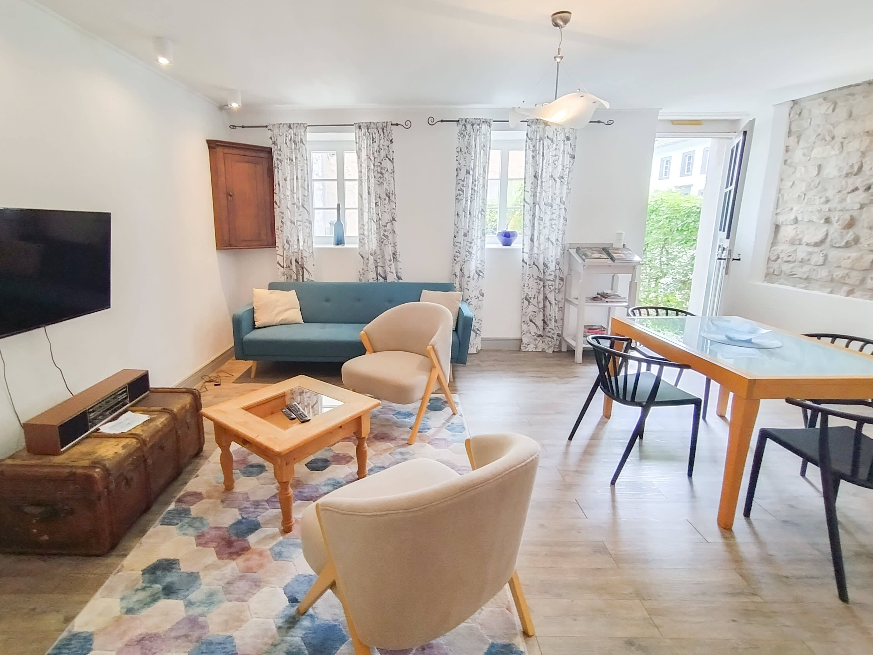 Un salon comprenant un canapé, des fauteuils, une table basse, un téléviseur, une table à manger avec des chaises et une fenêtre avec des rideaux.