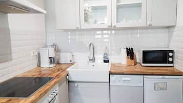 Une cuisine compacte avec des meubles blancs, un plan de travail en bois, un four à micro-ondes encastré, une machine à café et un lave-vaisselle.