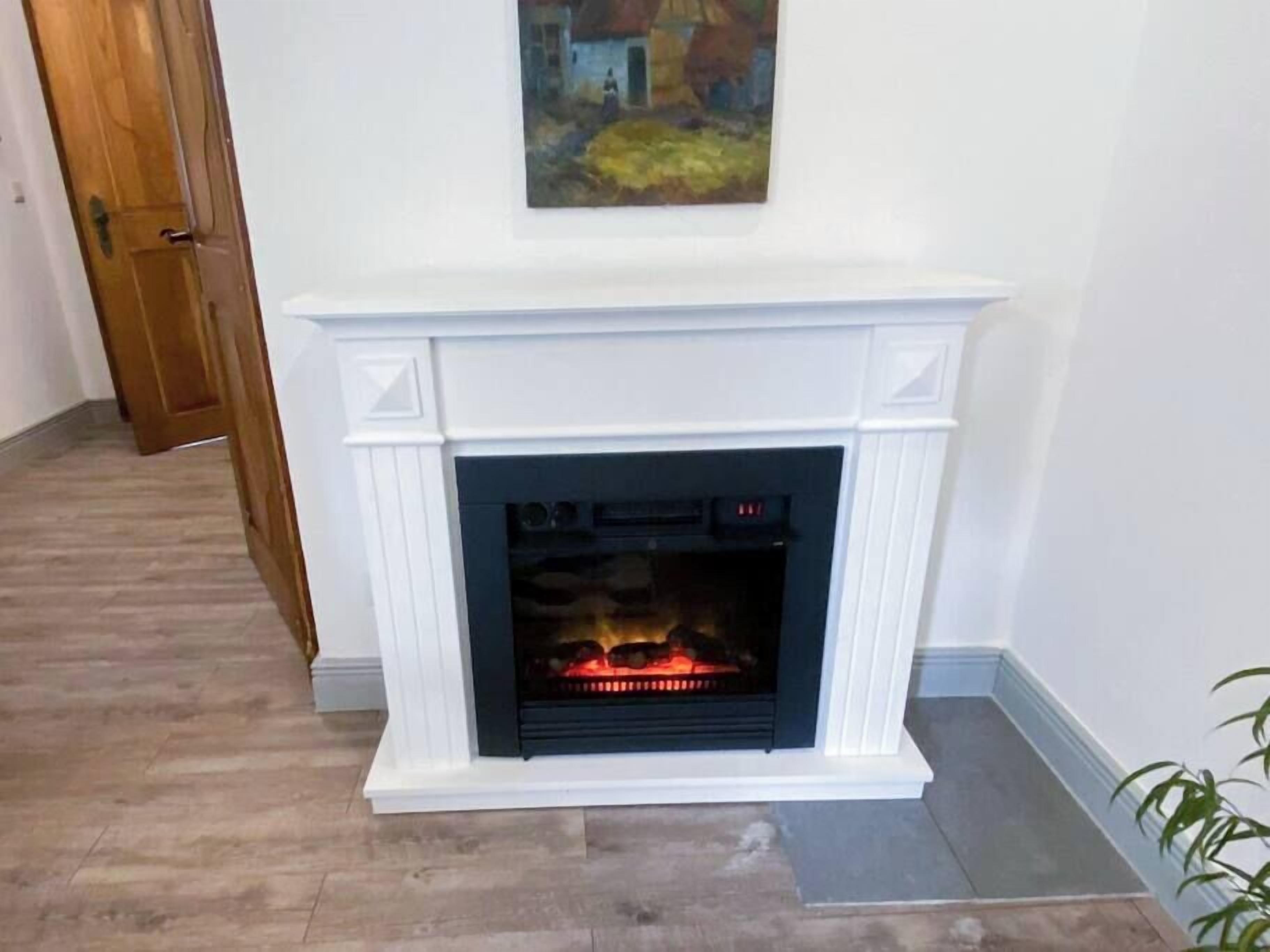 A fireplace with a white mantel and a modern design, located in a room with wooden flooring and a door in the background.