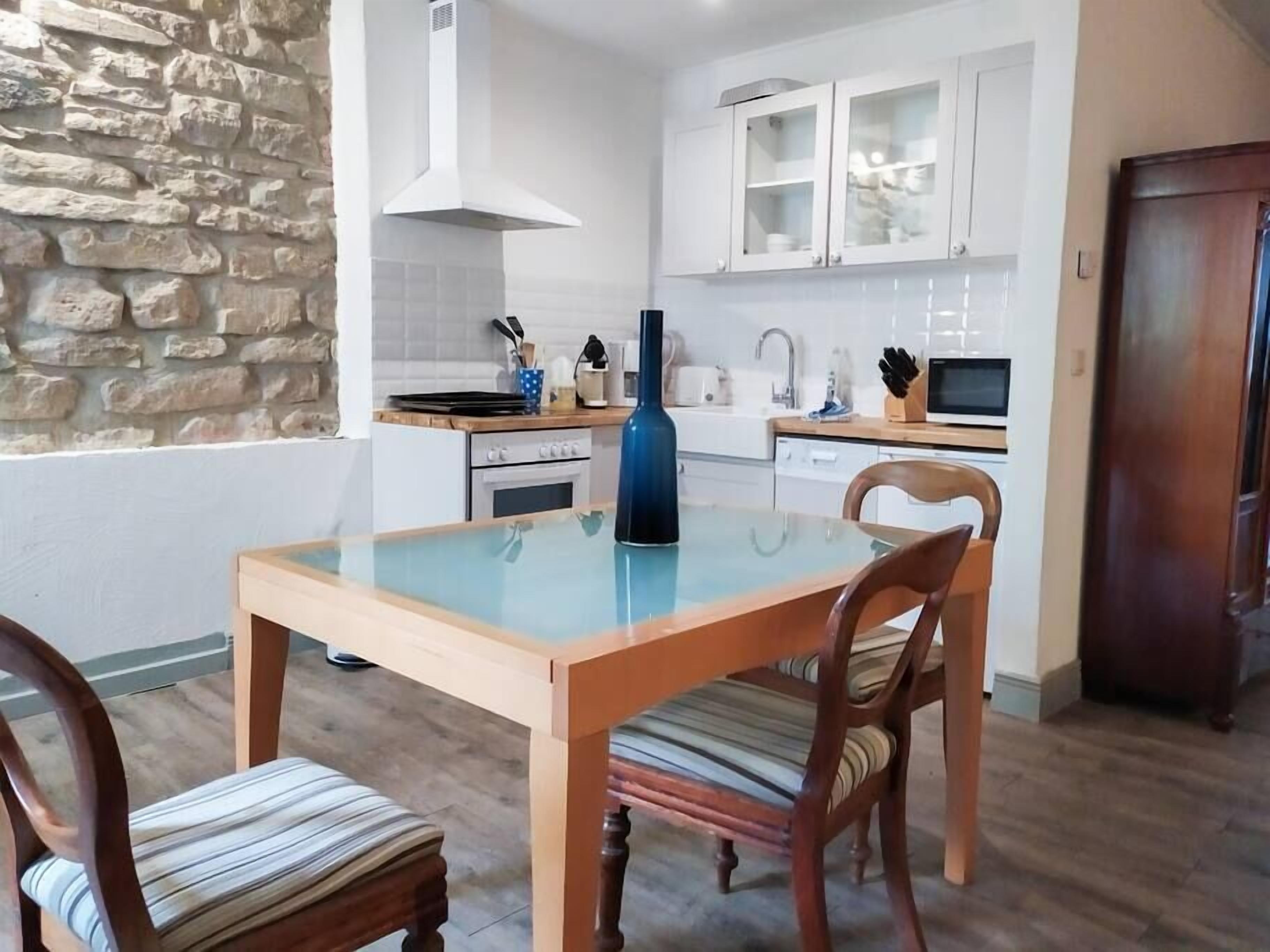 A modern kitchen with white cabinets, a stone wall, and a dining table with chairs.