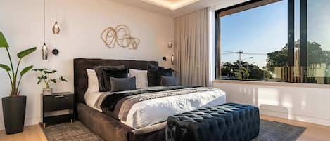 A modern bedroom with a large bed, bedside tables, a potted plant, and a view of the outdoors.