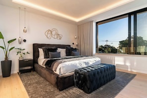 Ein modernes Schlafzimmer mit einem großen Bett, Nachttischen, einer Topfpflanze und Blick ins Freie.