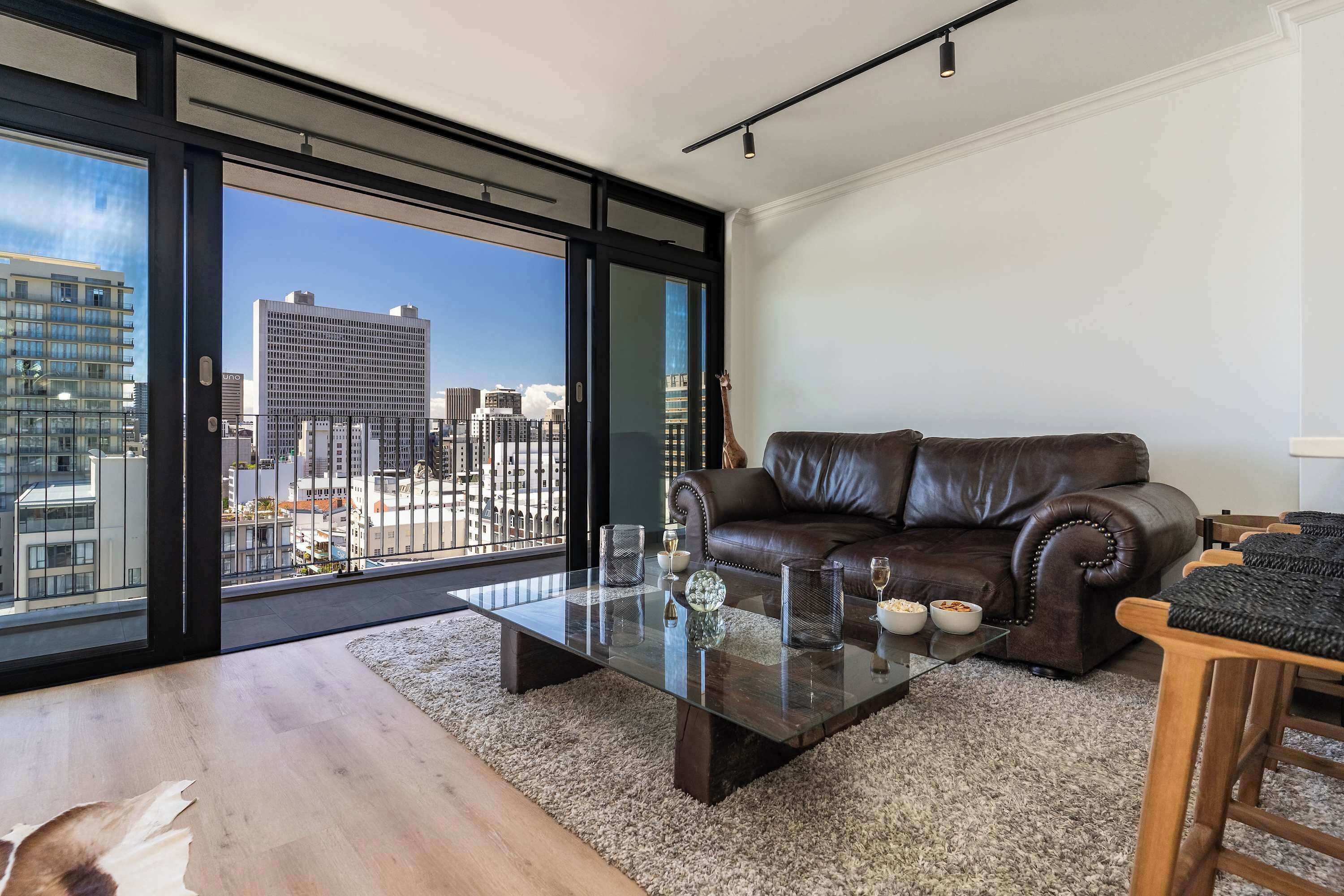 A modern living room with a leather sofa, a glass coffee table, and a view of the cityscape through large windows.