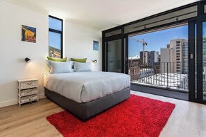 A modern bedroom with a large bed, a red rug, and a balcony with a city view. - City Views, Shared Gym, Cape Town -York Cityscape Apt (Cape Town)