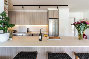 A modern kitchen with wooden cabinets, a stainless steel refrigerator, a wine bottle, and a glass of wine on the counter. - City Views, Shared Gym, Cape Town -York Cityscape Apt (Cape Town)