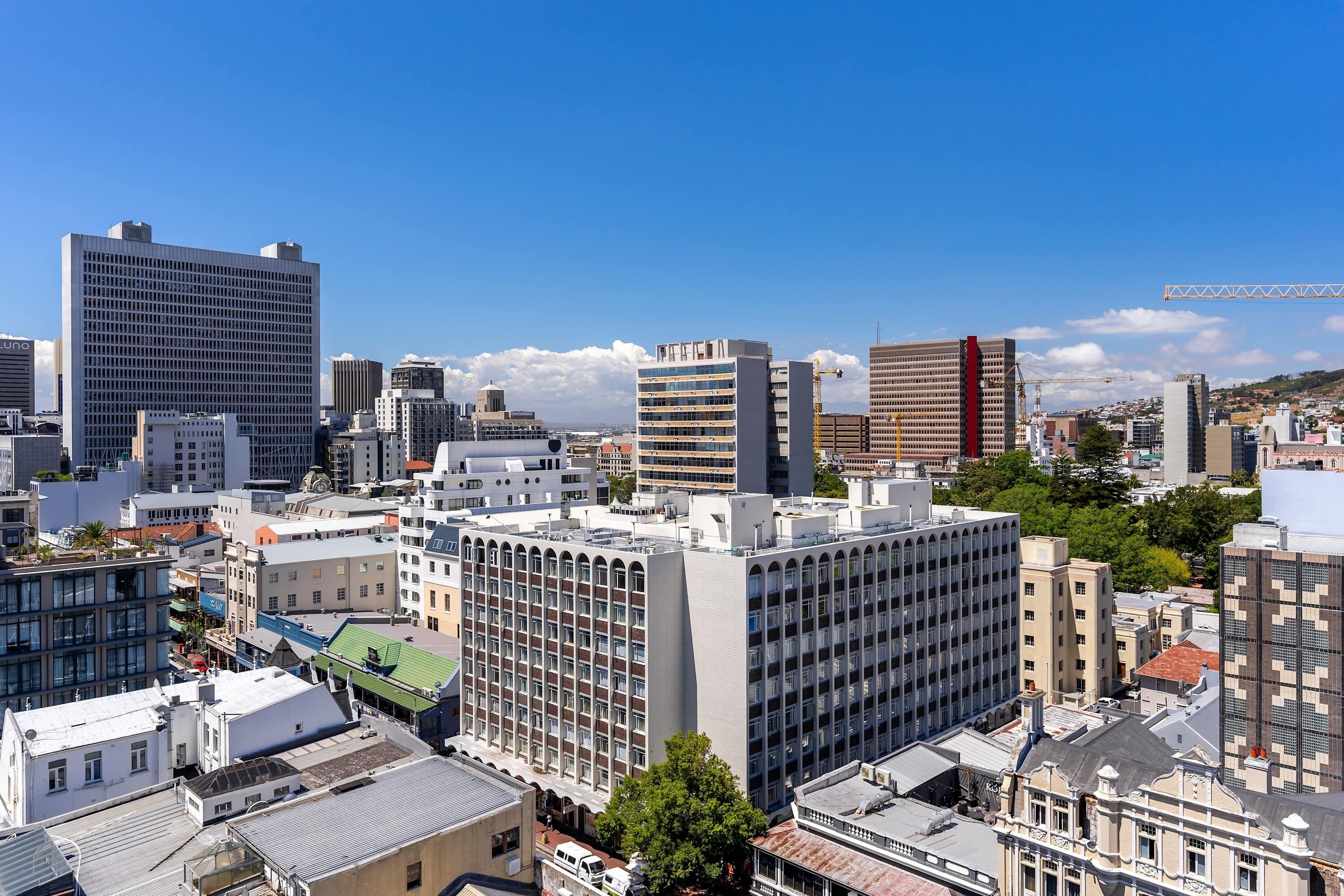 Paisagem urbana com diversos edifícios, incluindo um prédio branco de destaque com padrão quadriculado e um prédio vermelho com uma grua ao fundo.