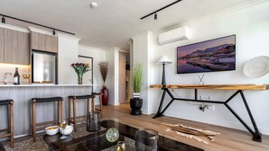 A modern kitchen with a built-in refrigerator, wooden cabinets, and a bar area. There is a dining table with chairs, a vase with flowers, and a lamp on a side table. - City Views, Shared Gym, Cape Town -York Cityscape Apt (Cape Town)