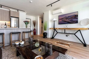 A modern kitchen with a built-in refrigerator, wooden cabinets, and a bar area. There is a dining table with chairs, a vase with flowers, and a lamp on a side table. - City Views, Shared Gym, Cape Town -York Cityscape Apt (Cape Town)