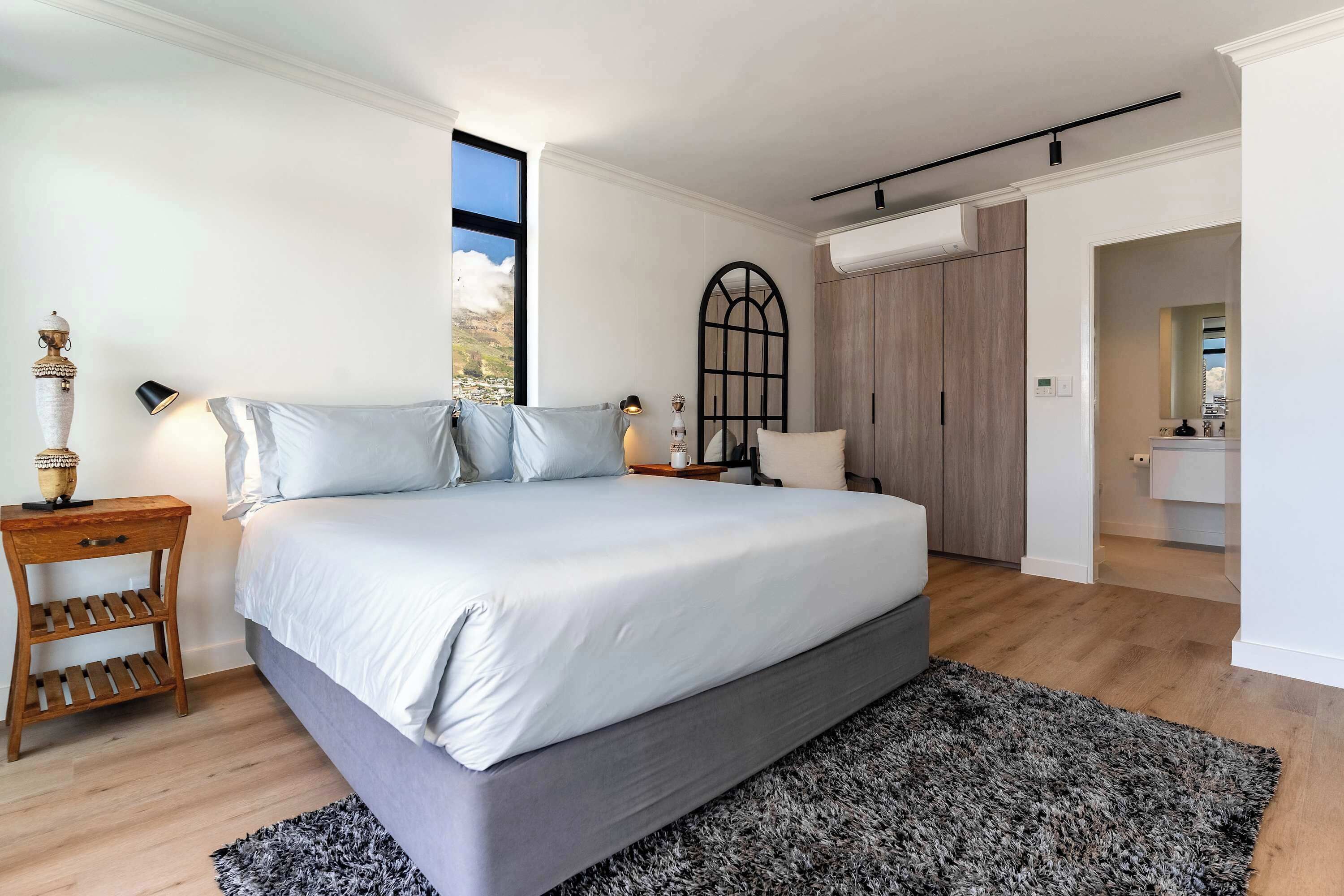 Ein Schlafzimmer mit einem großen Bett, Nachttischen aus Holz, einer schwarzen Lampe, einem Fenster und einem Kleiderschrank.
