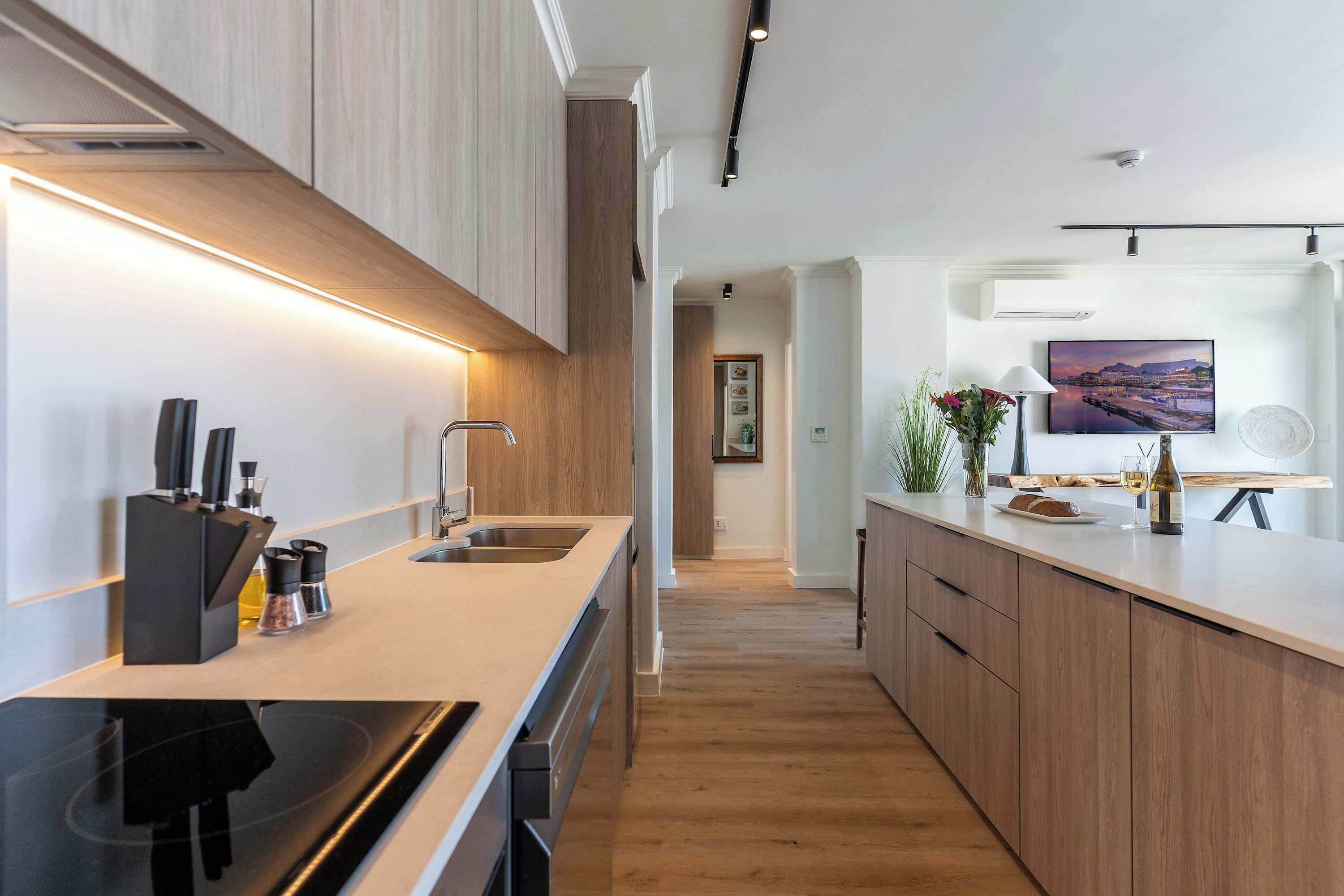 A modern kitchen with a long countertop, wooden cabinets, and a view into the dining area.