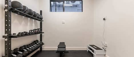Un gimnasio con racks de pesas, mancuernas, una banca y una ventana.