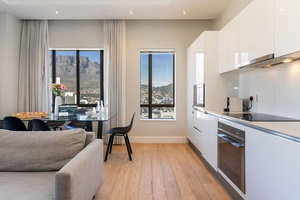 A modern kitchen with a view of a cityscape, a dining area with a table and chairs, and a sofa.