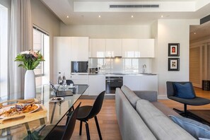 Eine moderne Küche mit weißen Schränken, ein Essbereich mit einem Glastisch und ein graues Sofa.