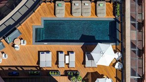 Vista aérea de uma área de piscina no terraço, com espreguiçadeiras, guarda-sóis e uma piscina.