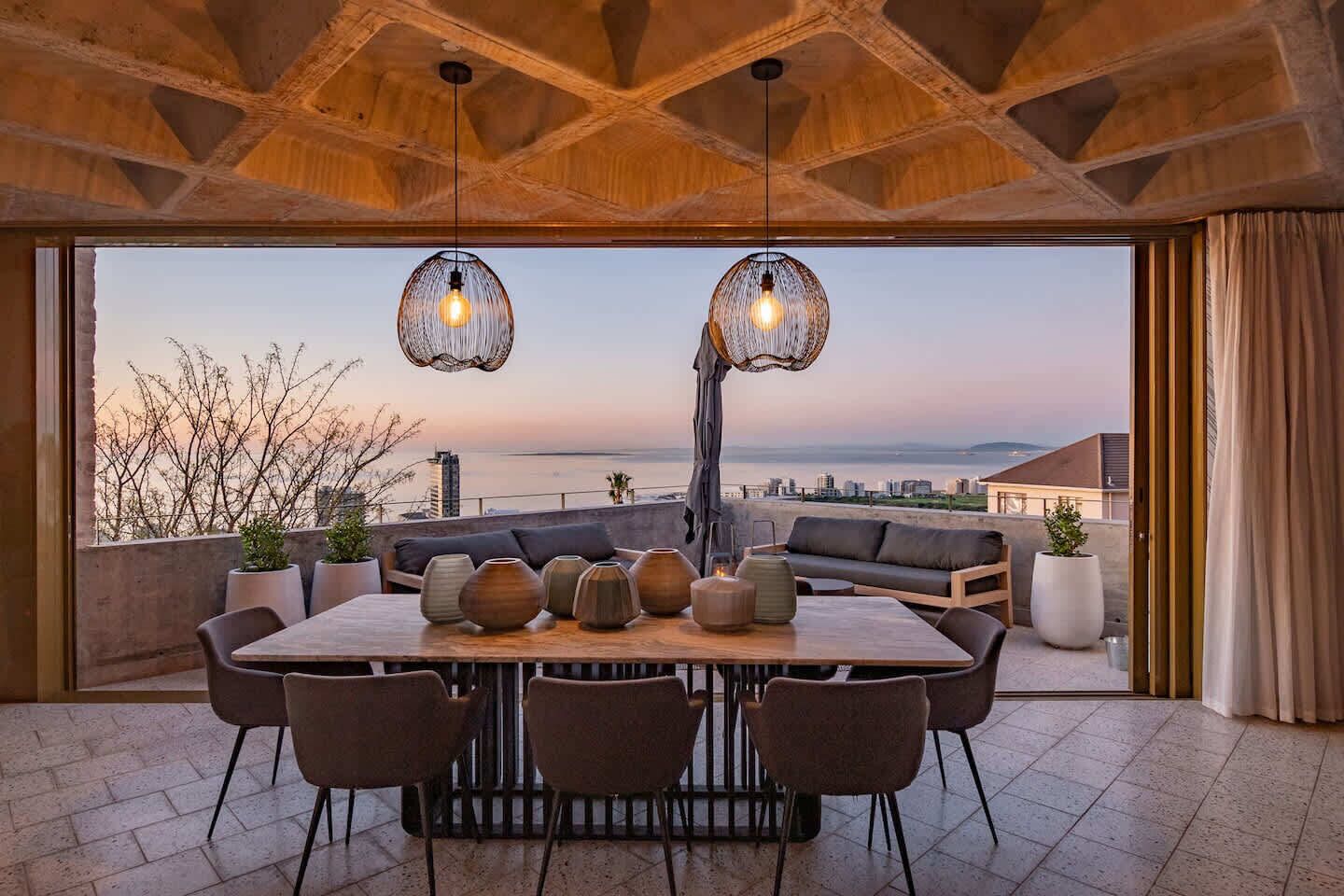 Eine Dachterrasse mit Holzboden, einem Esstisch mit Stühlen und hängenden Lampen.