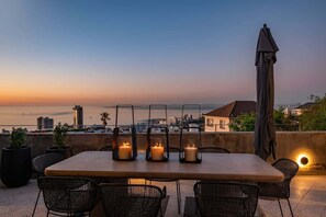 A rooftop terrace with a table set for four, surrounded by wicker chairs, and three candles in lanterns. - Luxurious, Pool, Views, Sea Point - Luna Penthouse (Cape Town)