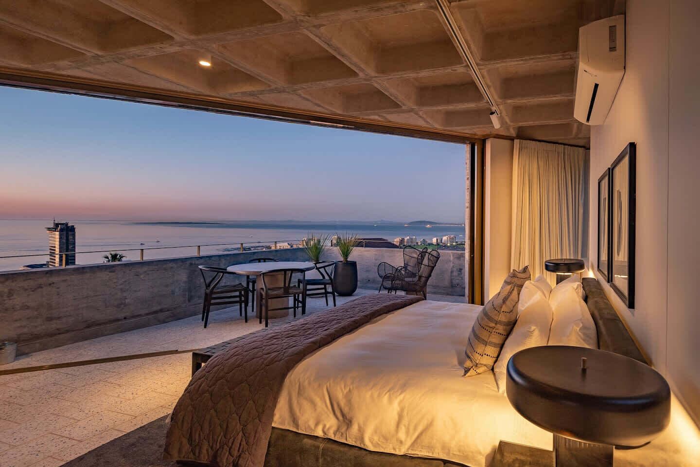 Quarto com cama grande, mesa de cabeceira, cadeira e vista para o mar.