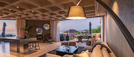 A spacious living area with a modern design, featuring a sofa, a coffee table, and a dining area with outdoor seating.