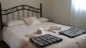 A neatly made bed with a black metal headboard, white bedding, and two folded towels. - AVE station at 10 min walking - Sostoa Apartment (Málaga)