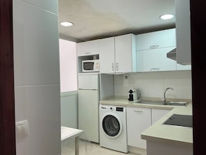 Een kleine keuken met een wasmachine, magnetron en spoelbak.