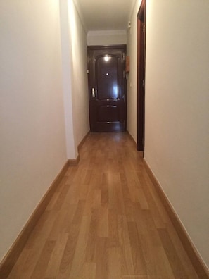 Ein schmaler Korridor mit Holzdielen und einer dunklen Tür am Ende.