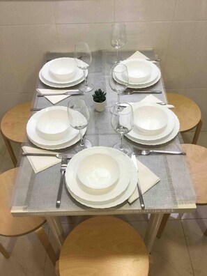 Ein Esstisch für sechs Personen, gedeckt mit weißen Tellern, Besteck und Gläsern, umgeben von Holzstühlen.